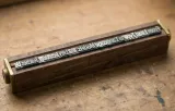 Mirror-image metal type in a wooden holder with brass ends on a worn, ink-stained workbench, spelling out the article title “From Lead Type to Language Models”